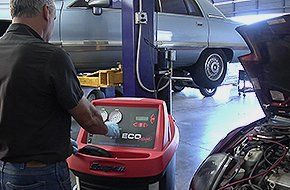 auto technician with a diagnostic computer hooked up to a car with the hood up