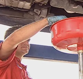 mechanic checking a red oil pan underneath a car on a auto lift in a repair bay